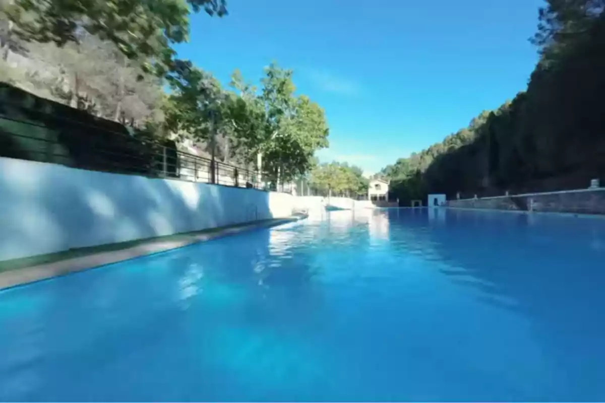 Piscina a l’aire lliure envoltada d’arbres i muntanyes sota un cel serè Piscina a l’aire lliure envoltada d’arbres i muntanyes sota un cel serè