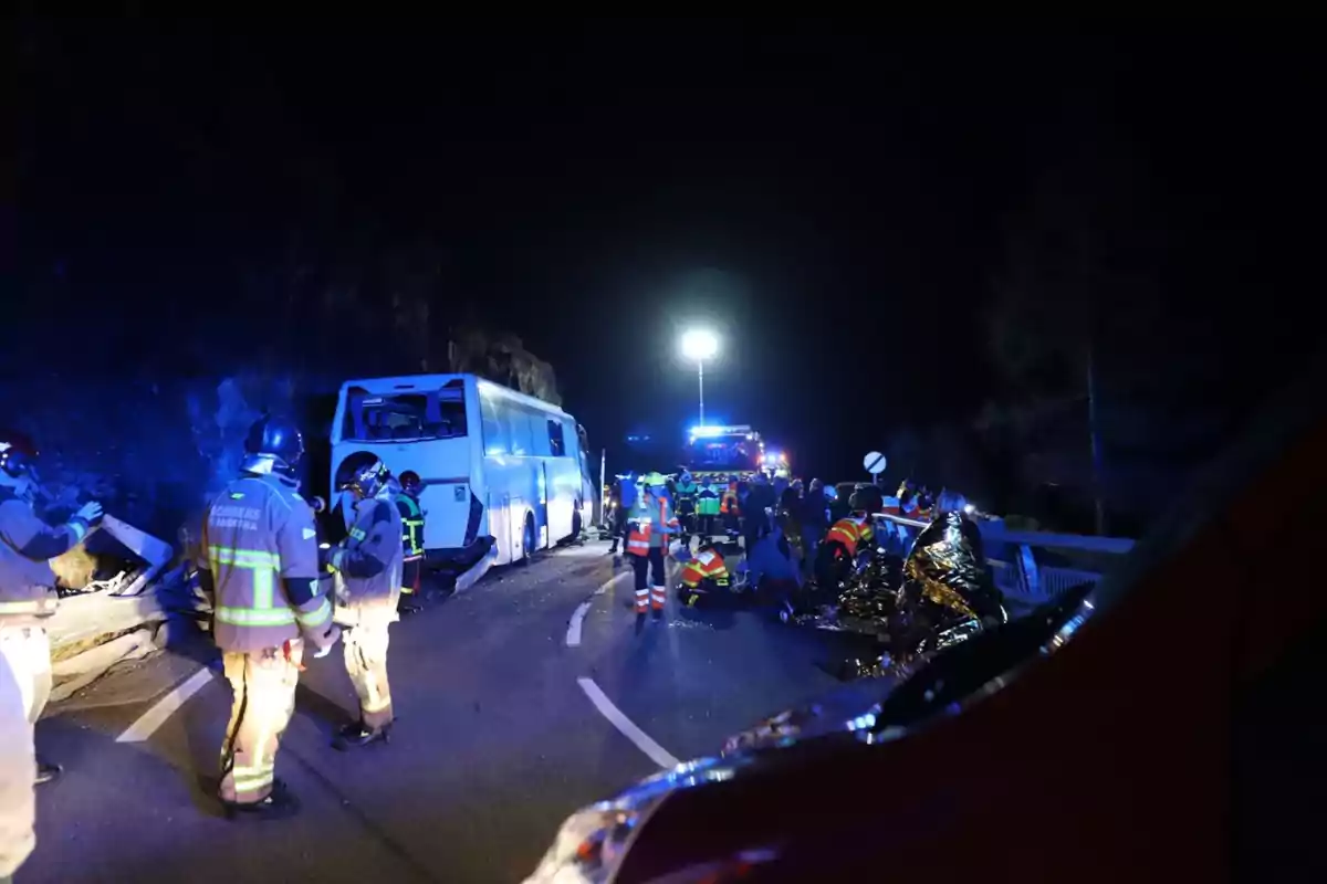 Accidente de autobús en carretera de noche con bomberos y equipos de emergencia trabajando en el lugar.