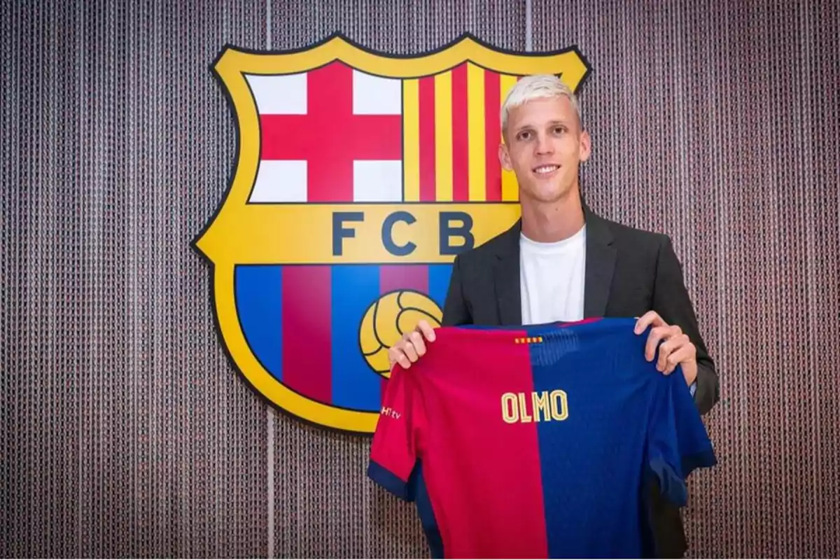 Un home sostenint una samarreta de futbol amb el nom Olmo davant de l'escut del FC Barcelona.