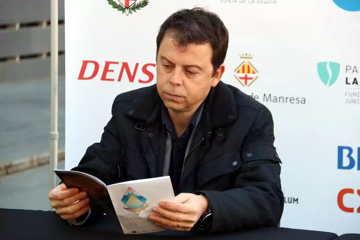 Un hombre sentado leyendo un folleto en un evento al aire libre.