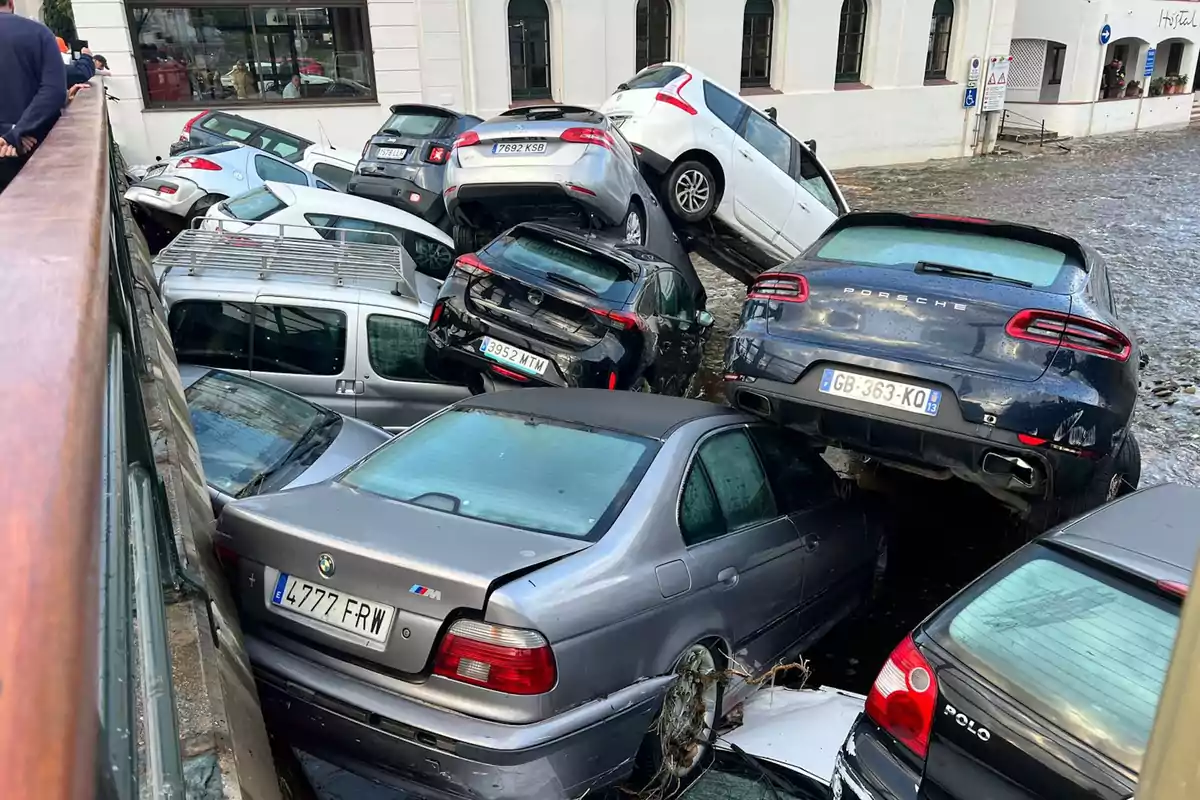 Varios coches apilados y dañados tras una inundación en una calle urbana.