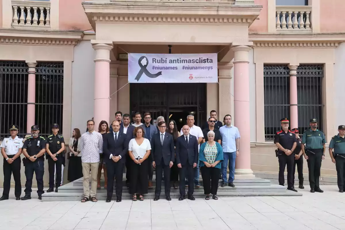 Un grup de persones, incloent oficials de policia, es troba davant d'un edifici amb columnes i un cartell que diu Un grup de persones, incloent oficials de policia, es troba davant d'un edifici amb columnes i un cartell que diu