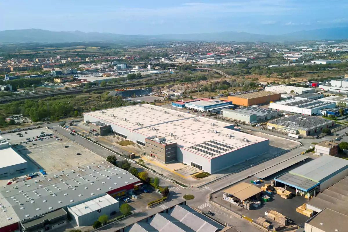 Vista aèria d´un parc industrial amb diversos edificis grans i un paisatge urbà al fons.