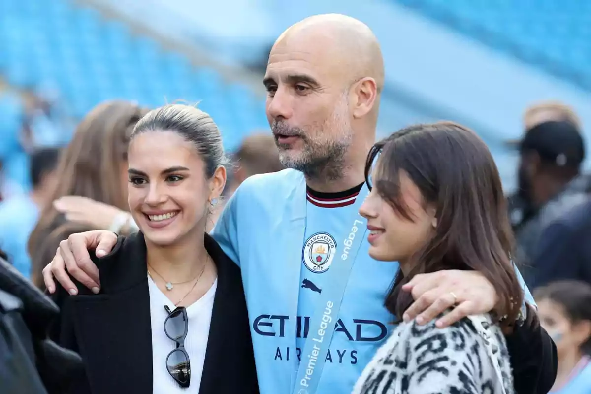 Un home amb una samarreta de futbol del Manchester City, amb dues dones en un estadi.