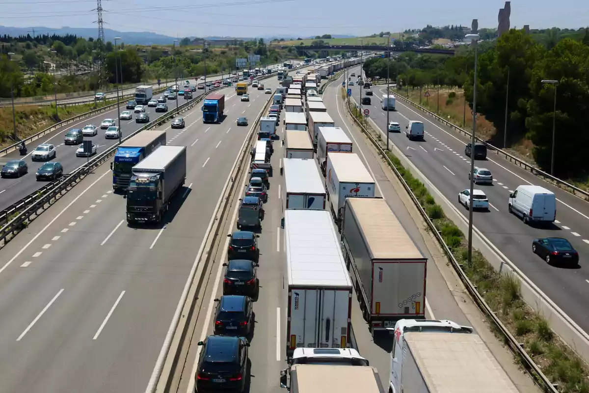 Trànsit dens a una autopista amb una fila de camions i cotxes en un carril mentre l'altre carril té trànsit fluid.