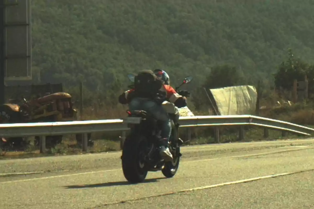 Una motocicleta amb dues persones circula per una carretera envoltada de vegetació i muntanyes.