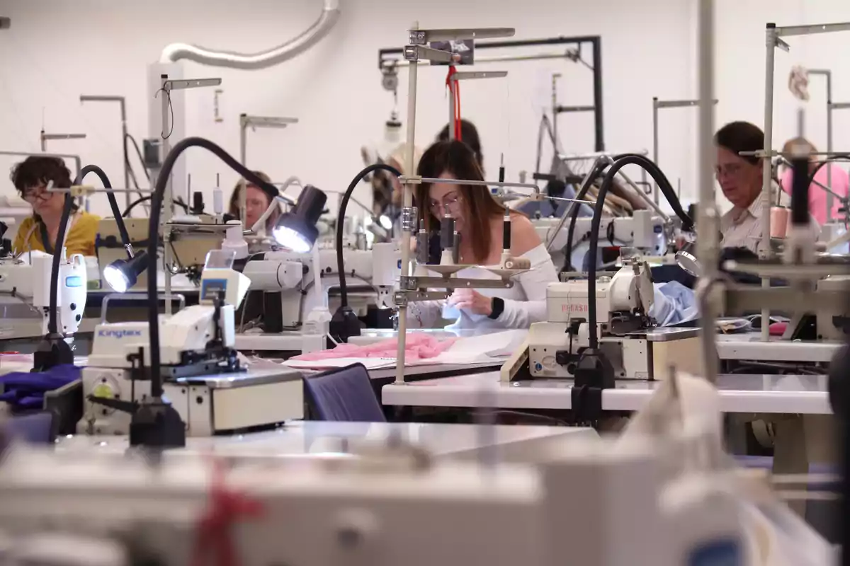 Personas trabajando en una fábrica de costura con varias máquinas de coser.