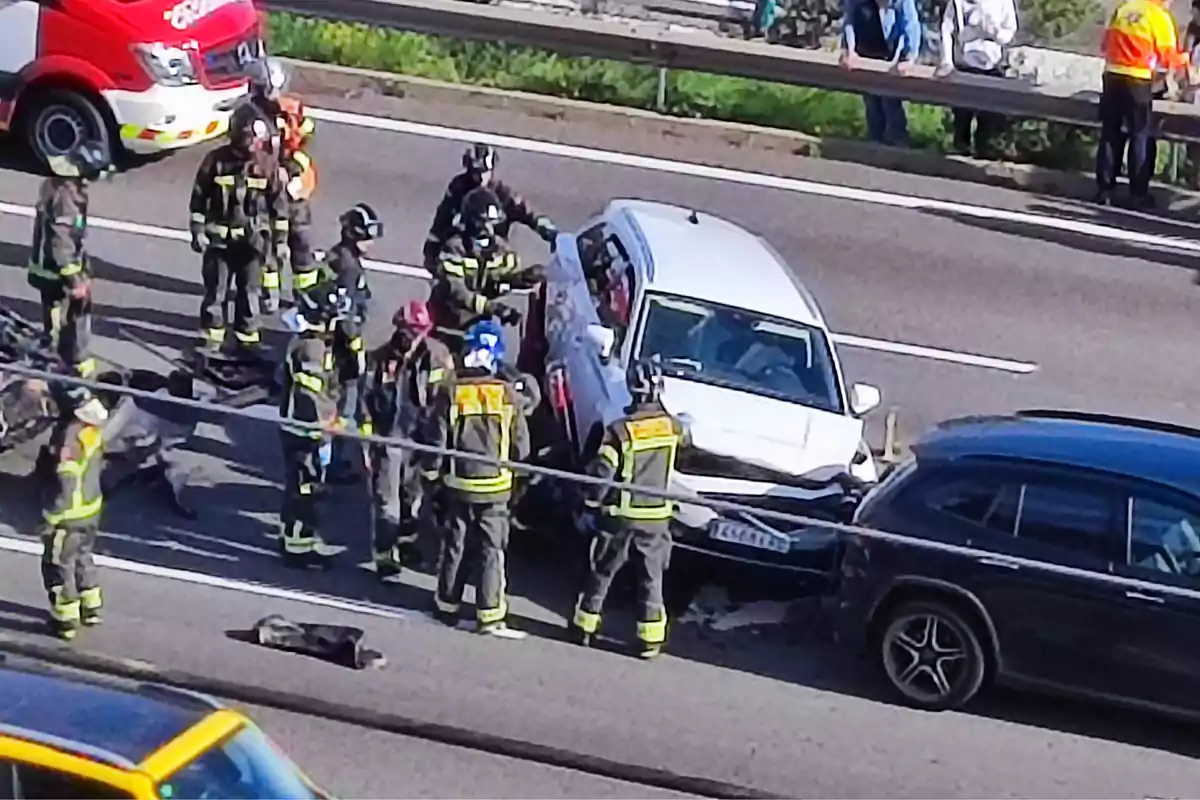 Un grup de bombers atén un accident de trànsit a una carretera, on dos vehicles han col·lisionat i s'observa un camió de bombers al fons.