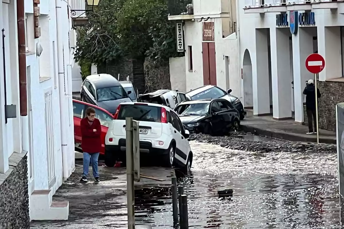 Una calle inundada con varios coches dañados y una persona caminando por la acera.