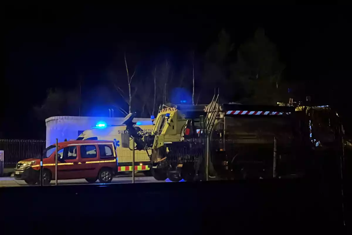 Vehículos de emergencia y maquinaria pesada iluminados por luces azules en la noche.