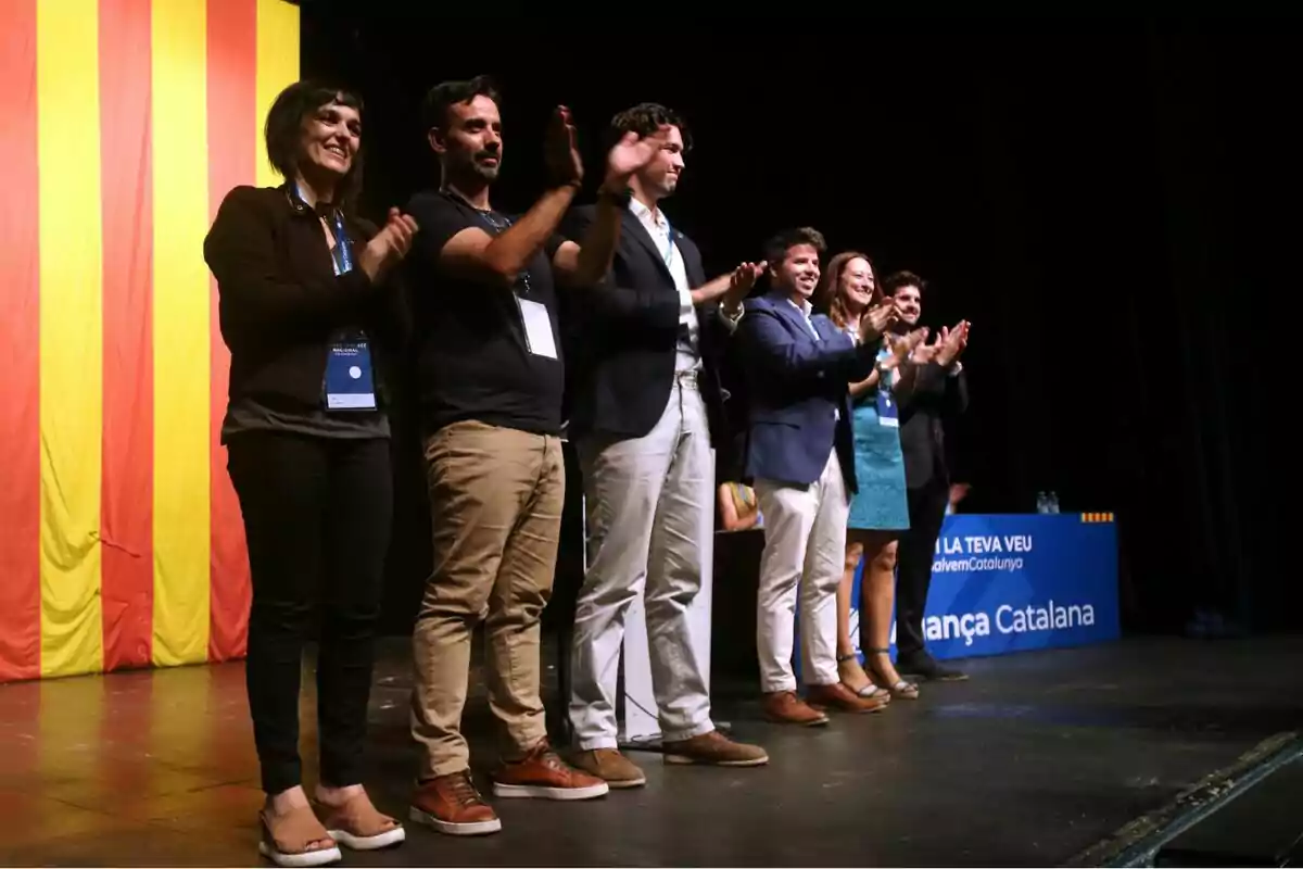 Un grup de persones aplaudint en un escenari amb una bandera catalana de fons.