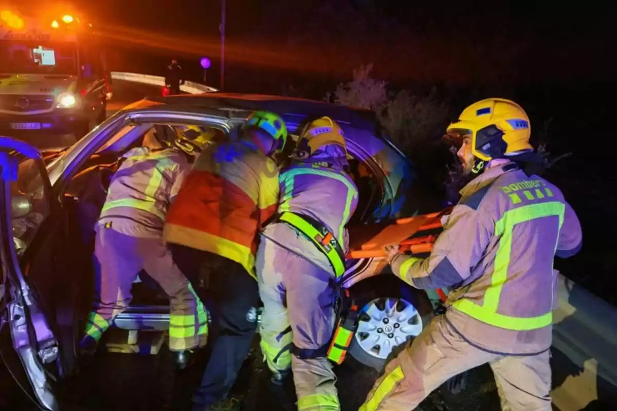 Bomberos rescatan a una persona de un vehículo accidentado en una carretera durante la noche con una ambulancia en el fondo.