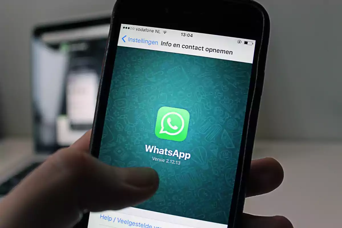 Una mano sostiene un teléfono móvil que muestra la pantalla de inicio de la aplicación WhatsApp.