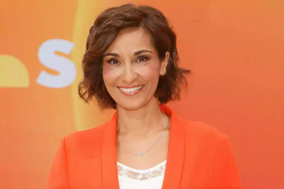 Adela González sonriente con cabello corto y ondulado, vestida con una chaqueta naranja, posando frente a un fondo naranja en Mañaneros Adela González sonriente con cabello corto y ondulado, vestida con una chaqueta naranja, posando frente a un fondo naranja en Mañaneros