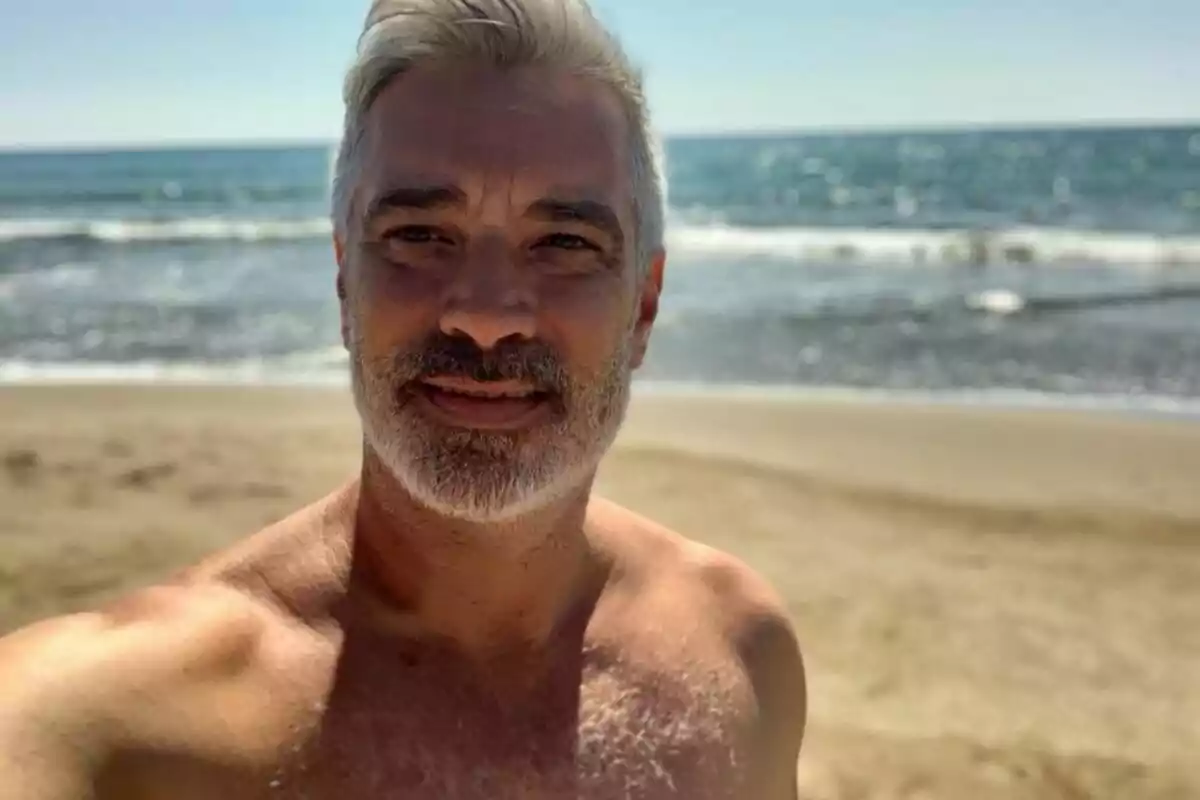 Hombre de cabello canoso y barba en la playa con el mar de fondo.