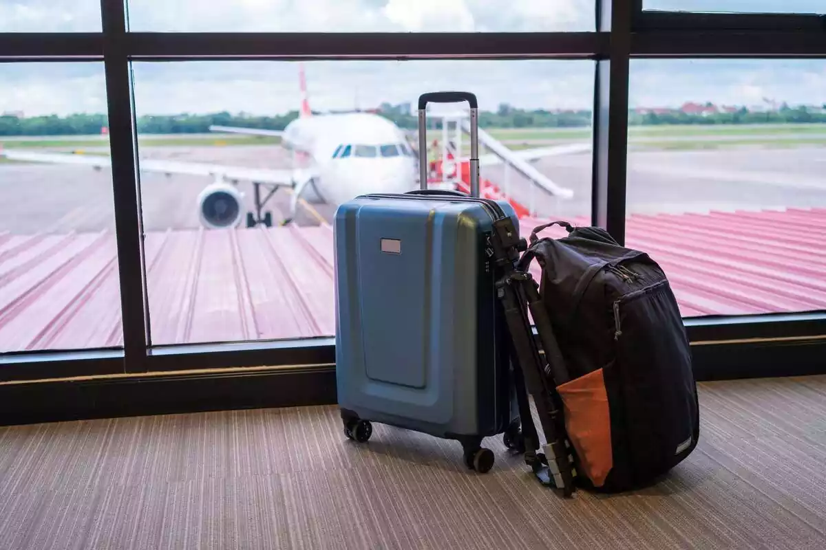 Maletes davant la finestra d'un aeroport on es veu un avió aparcat Maletes davant la finestra d'un aeroport on es veu un avió aparcat