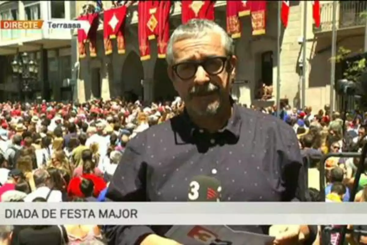 Un reporter cobreix un esdeveniment multitudinari a una plaça decorada amb banderes vermelles durant la Diada de Festa Major a Terrassa.