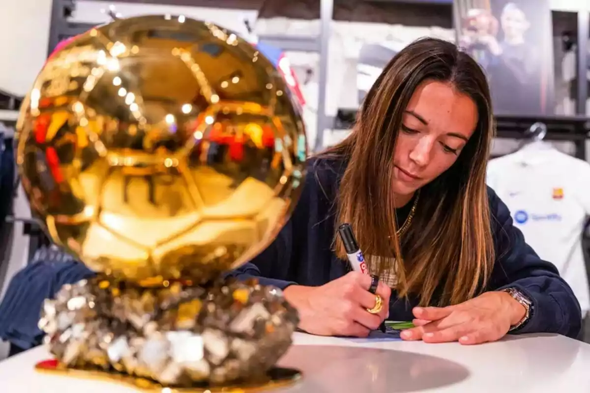 Una mujer firmando un autógrafo junto a un trofeo dorado.