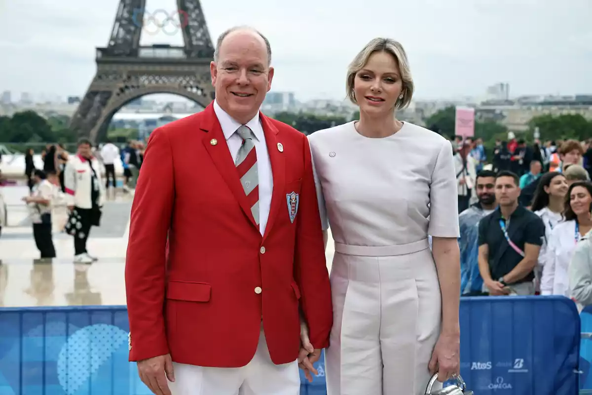 Albert of Monaco and Charlene pose in front of the Eiffel Tower, one of them wearing a red suit and the other a white outfit, surrounded by a group of people with a cloudy sky in the background. Albert of Monaco and Charlene pose in front of the Eiffel Tower, one of them wearing a red suit and the other a white outfit, surrounded by a group of people with a cloudy sky in the background.