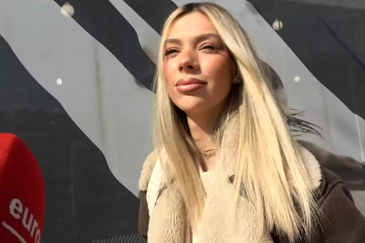 Alejandra Rubio con abrigo claro está al aire libre frente a un fondo oscuro y un micrófono rojo. Alejandra Rubio con abrigo claro está al aire libre frente a un fondo oscuro y un micrófono rojo.
