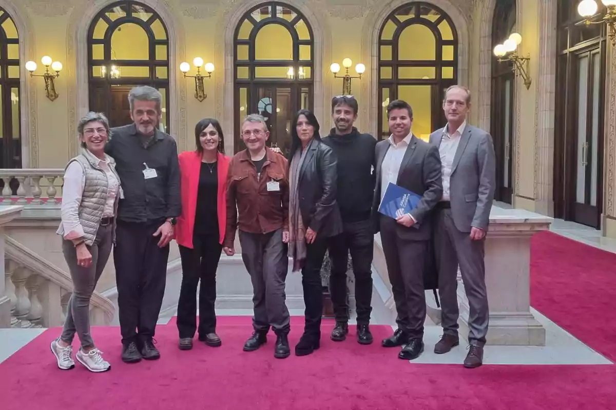 Un grup de persones posant en un edifici elegant amb catifa vermella i grans finestrals.