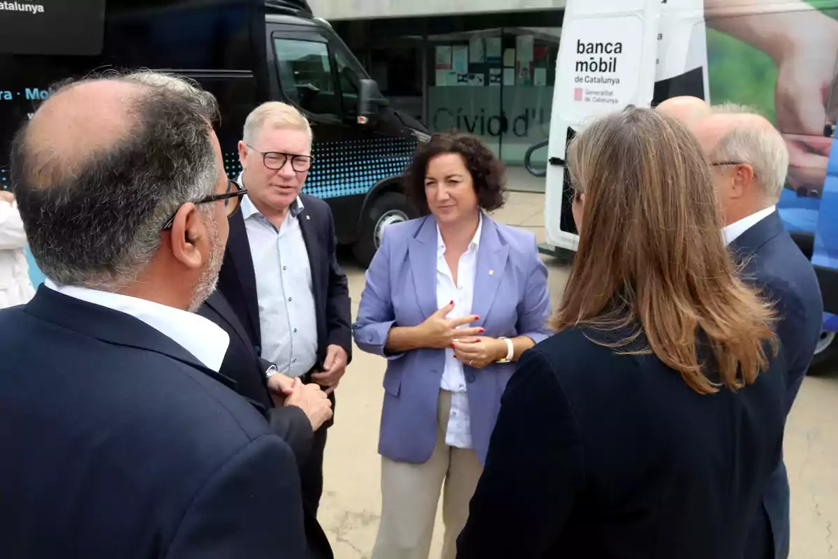 Un grupo de personas conversando frente a una unidad móvil de banca en Cataluña.