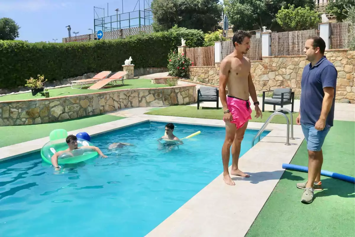 Varias personas disfrutan de una piscina en un día soleado, mientras dos hombres conversan en el borde de la piscina.