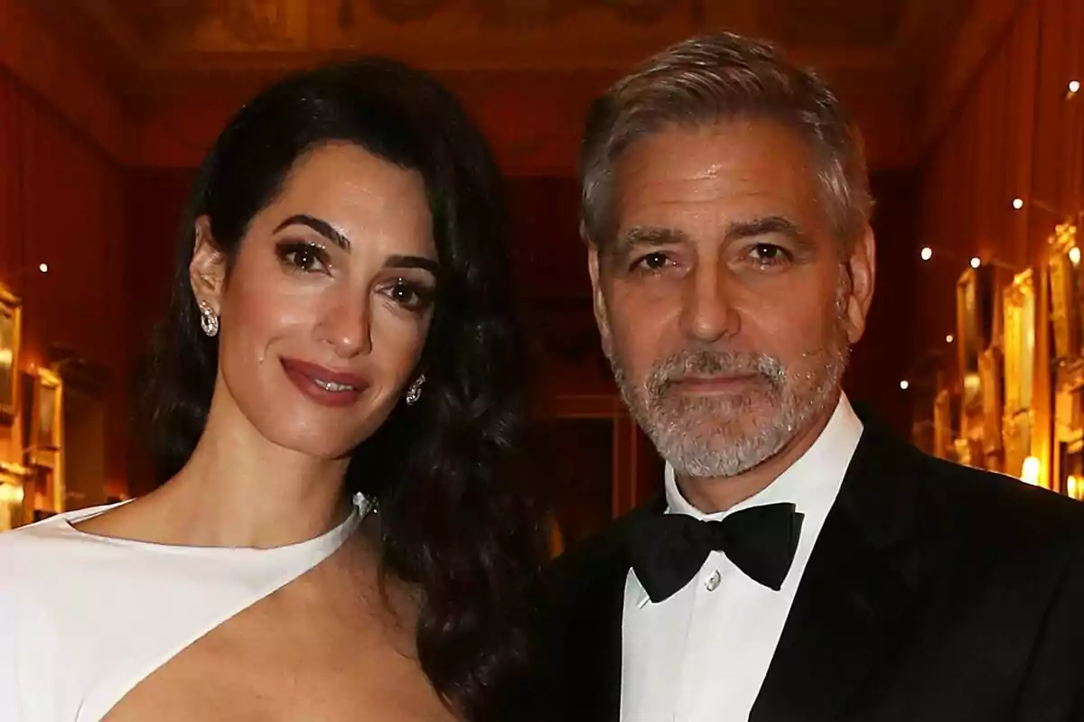 Amal i George Clooney elegantment vestits posen en un esdeveniment formal amb un fons d'il·luminació càlida i quadres a les parets. Amal i George Clooney elegantment vestits posen en un esdeveniment formal amb un fons d'il·luminació càlida i quadres a les parets.