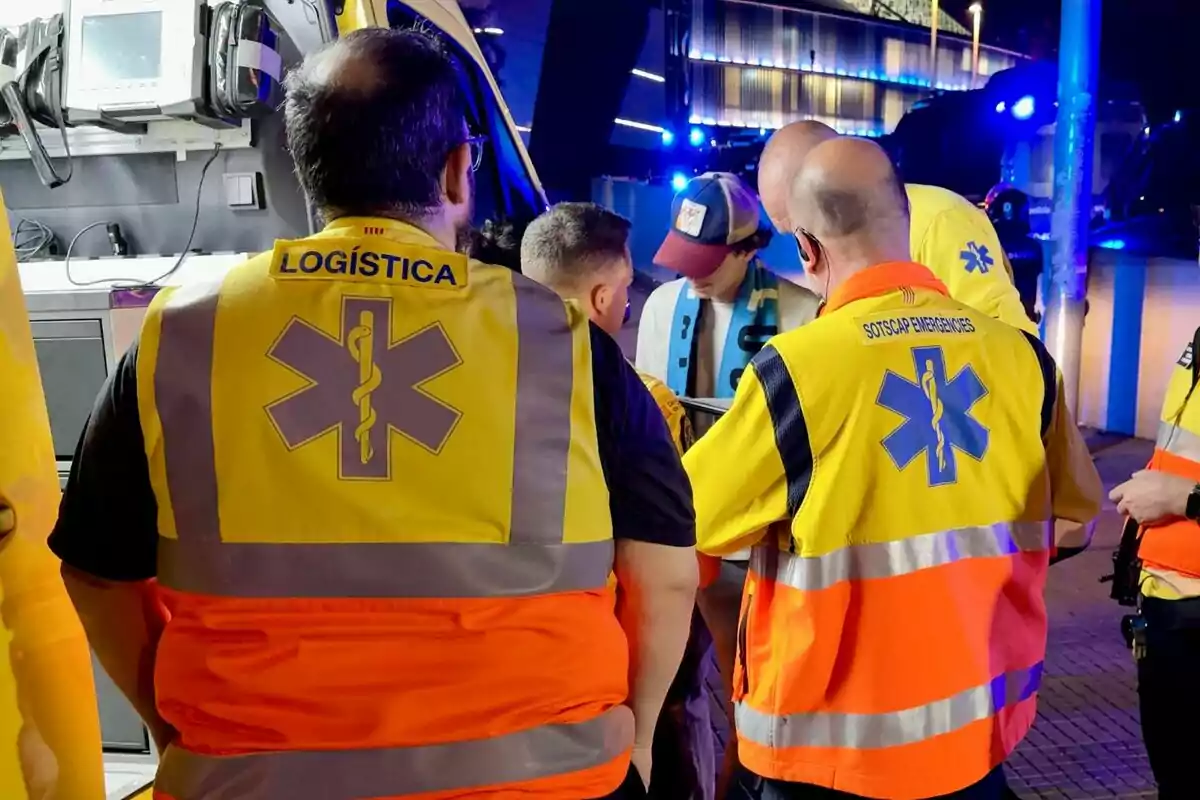 Persones amb armilles de logística i emergències conversen en un entorn il·luminat amb llums blaves. Persones amb armilles de logística i emergències conversen en un entorn il·luminat amb llums blaves.