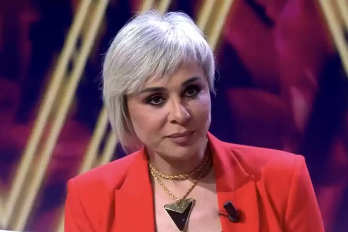 Ana María Aldón amb cabell curt i ros vestida amb un vestit vermell i un collaret daurat en un ambient il·luminat.