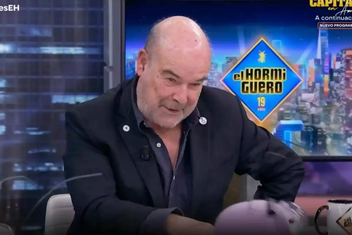 Un home calb amb barba està assegut en un estudi de televisió amb un fons que mostra el logotip d'un programa anomenat "El Hormiguero".