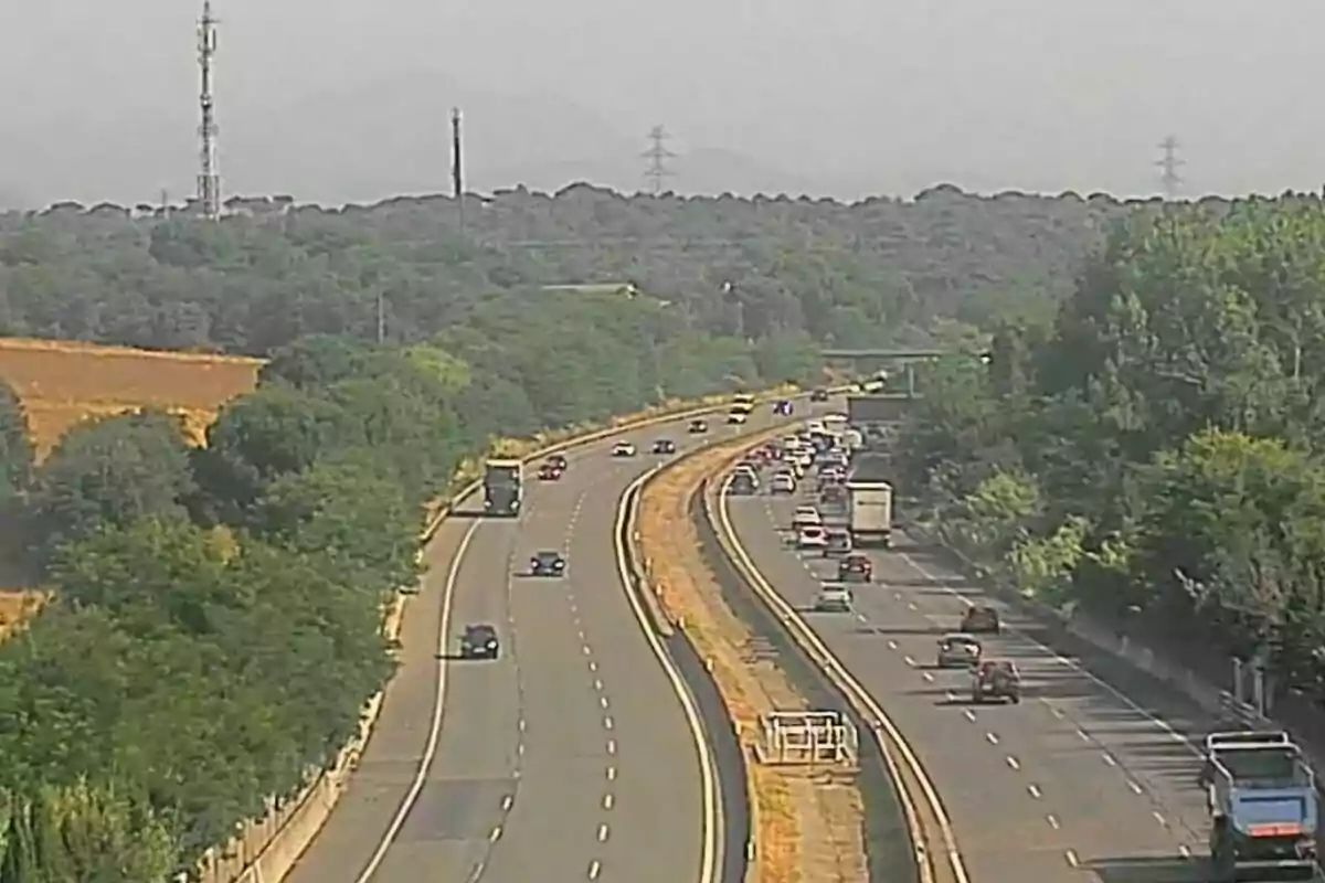 Carretera de diversos carrils envoltada d’arbres amb trànsit moderat i alguns camions i cotxes circulant en ambdues direccions