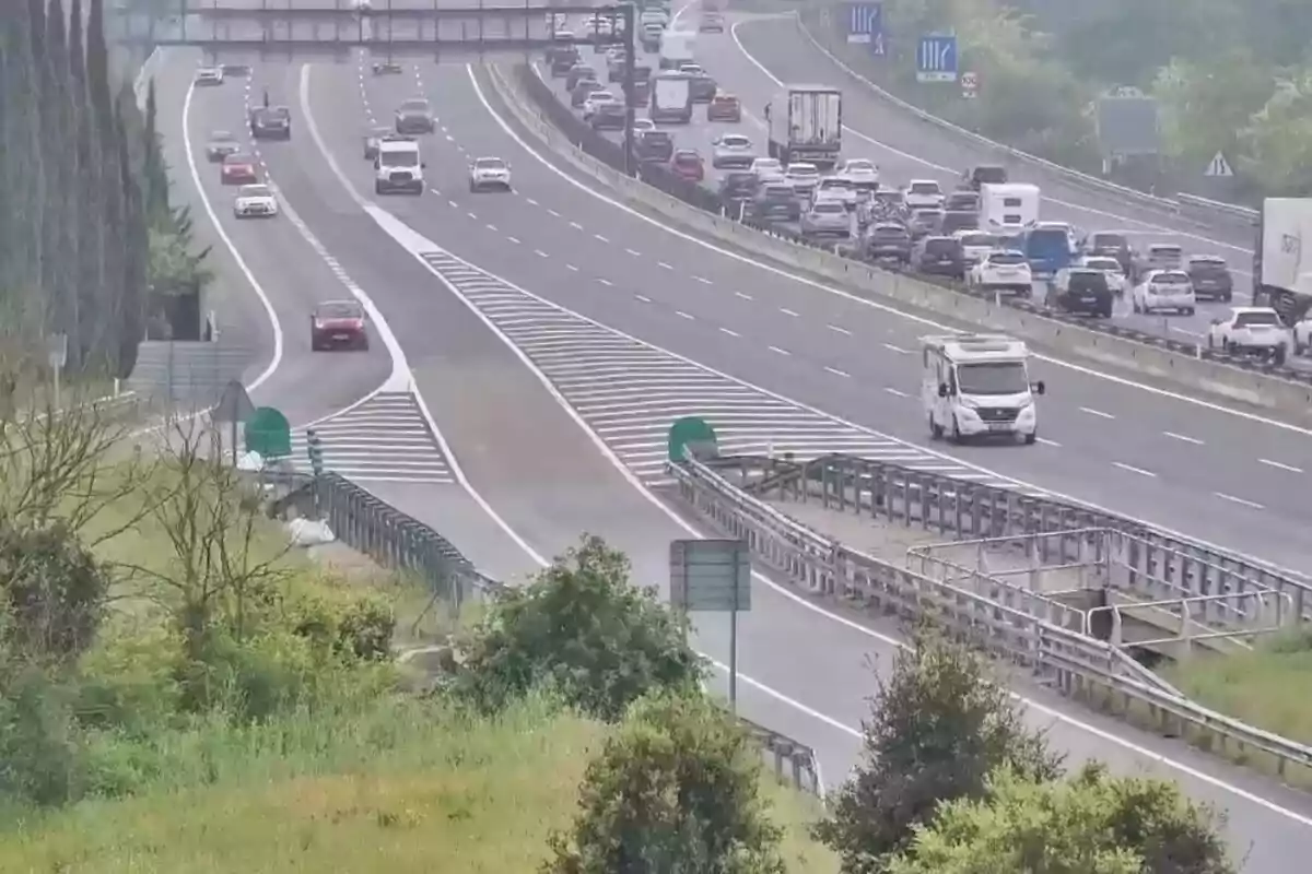 Una carretera con varios carriles donde se observa tráfico en una dirección y un vehículo blanco circulando en el carril de salida.