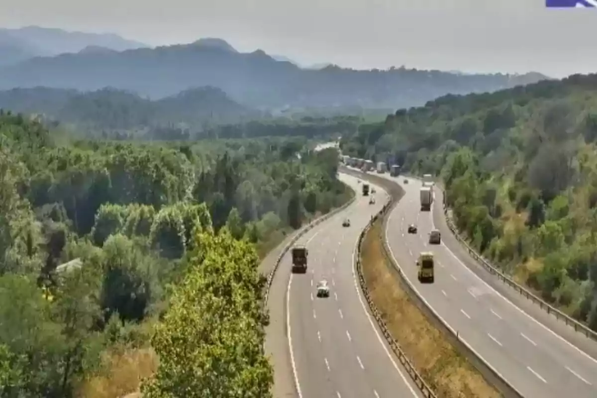 Carretera de diversos carrils envoltada d’arbres i muntanyes amb diversos vehicles circulant en ambdós sentits sota un cel serè