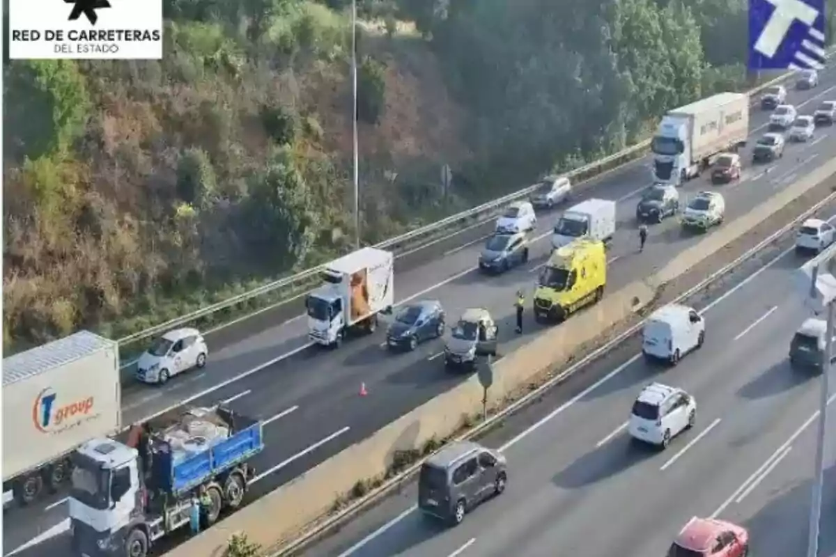 Trànsit aturat en una autopista a causa d’un accident, amb presència d’una ambulància groga, diversos vehicles aturats i agents de trànsit gestionant la situació.