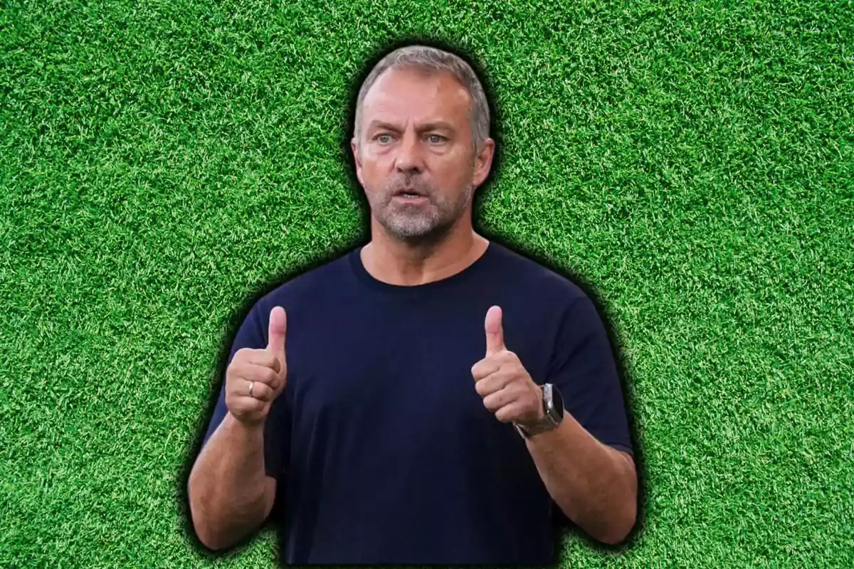 Un hombre con barba y cabello corto, vestido con una camiseta negra, está de pie frente a un fondo de césped verde, levantando ambos pulgares.