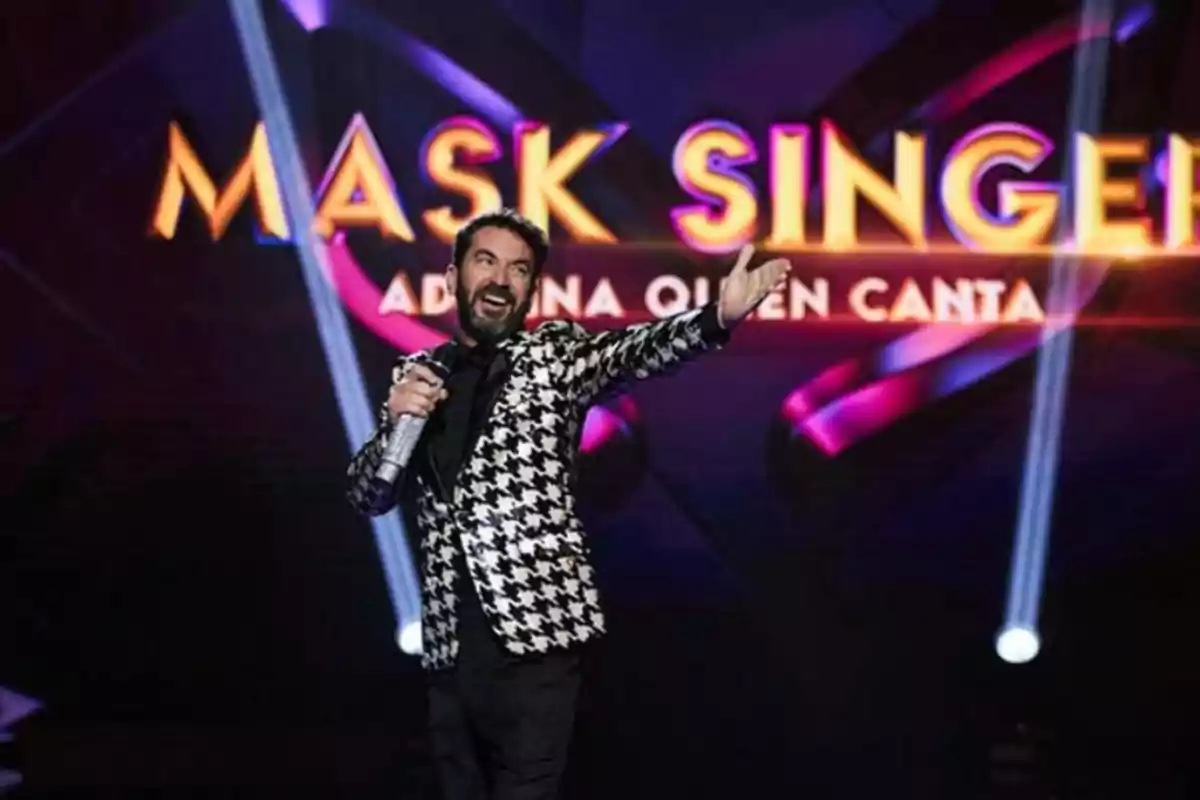 Smiling host with microphone in hand on the Mask Singer stage with a colorful background and bright lights Smiling host with microphone in hand on the Mask Singer stage with a colorful background and bright lights