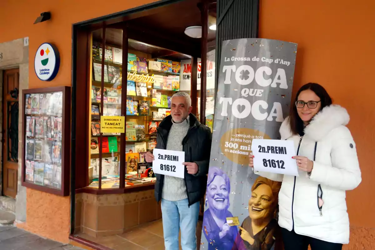 Dues persones sostenen cartells amb el número guanyador del segon premi de la loteria davant d'una botiga de loteria a Catalunya.