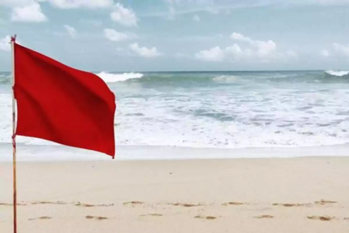 Bandera vermella onejant a la platja amb el mar de fons.