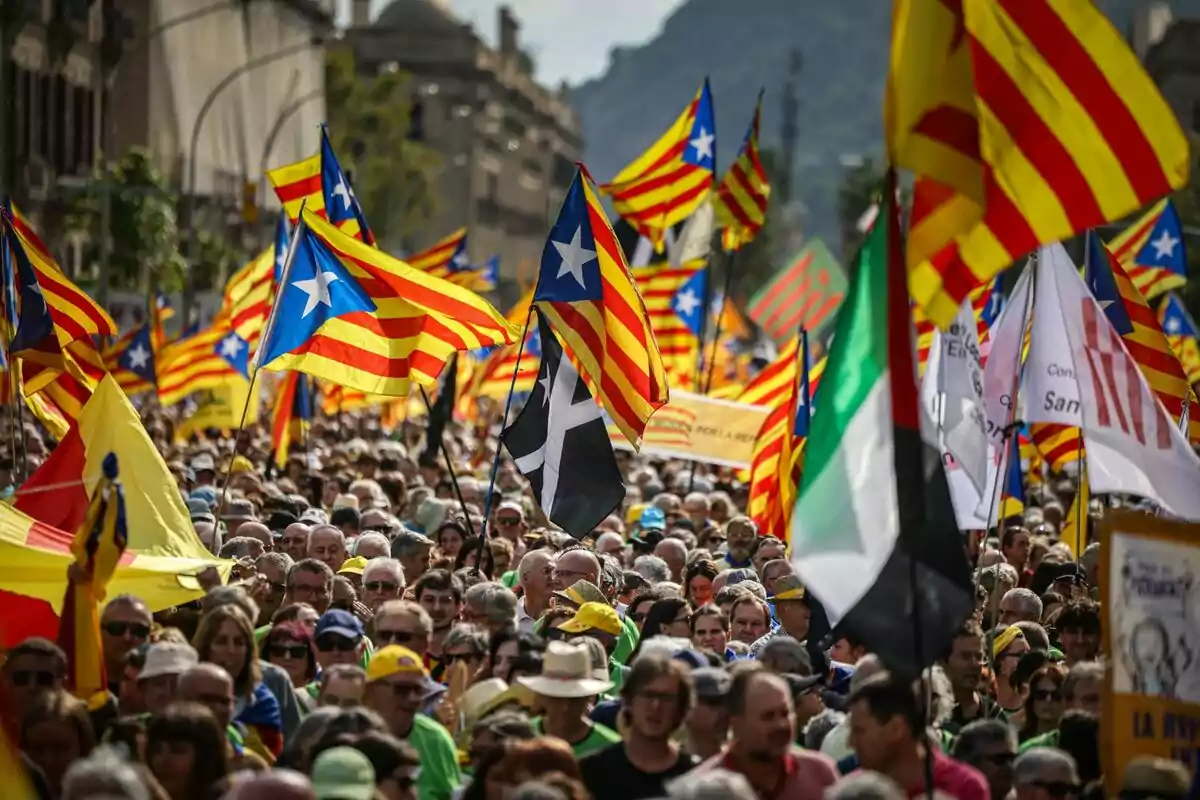 Una multitud de persones marxant amb nombroses banderes, principalment amb els colors groc i vermell, en una manifestació a una ciutat.