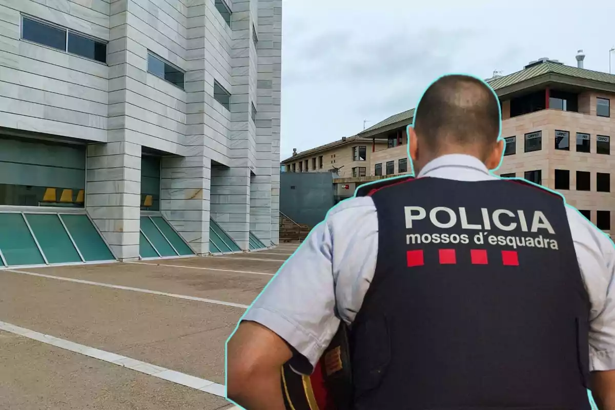 Un agent de policia d'esquena amb una armilla que diu "Policia Mossos d'Esquadra" davant d'un edifici modern amb finestres inclinades i parets de marbre.