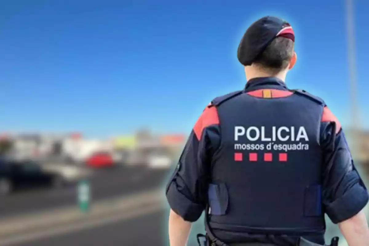 Policia d'esquena amb uniforme dels Mossos d'Esquadra a una carretera.