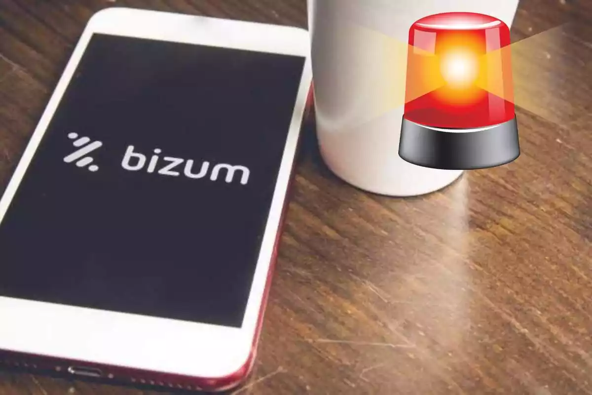 Muntatge amb smartphone amb la paraula i el logotip de Bizum damunt una taula. Senyal d'emergències a la part superior dreta