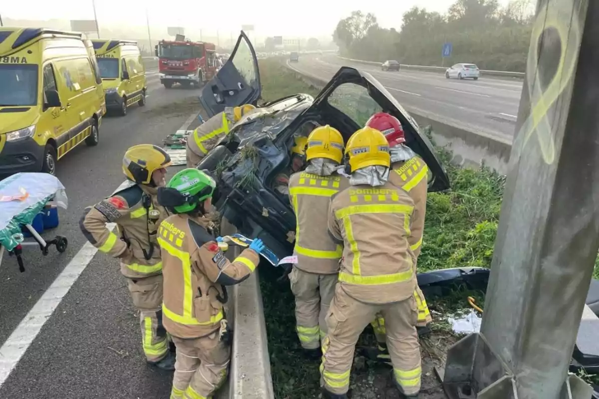 Bomberos trabajando en el rescate de un vehículo volcado en una carretera, con ambulancias y un camión de bomberos en el fondo.