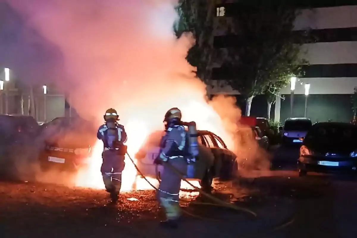 Bombers apagant un cotxe en flames en un aparcament a la nit.