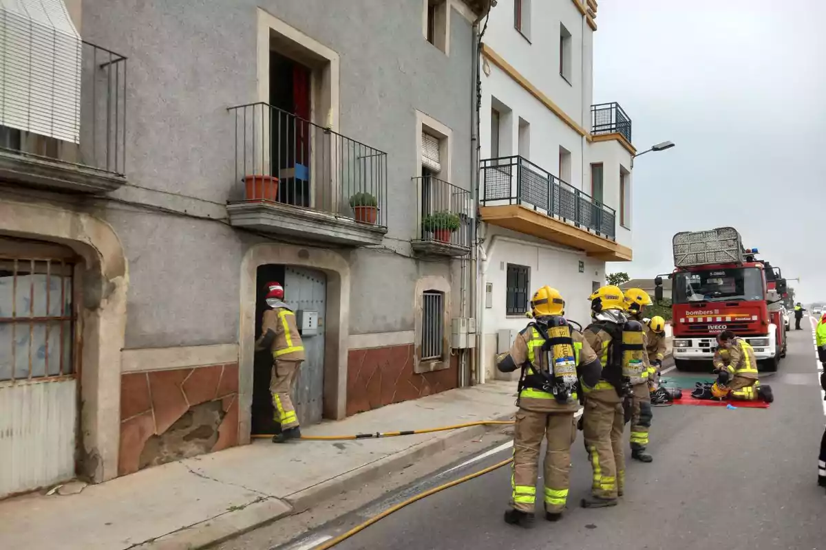 Bombers en acció davant d'un edifici, amb un camió de bombers estacionat al carrer