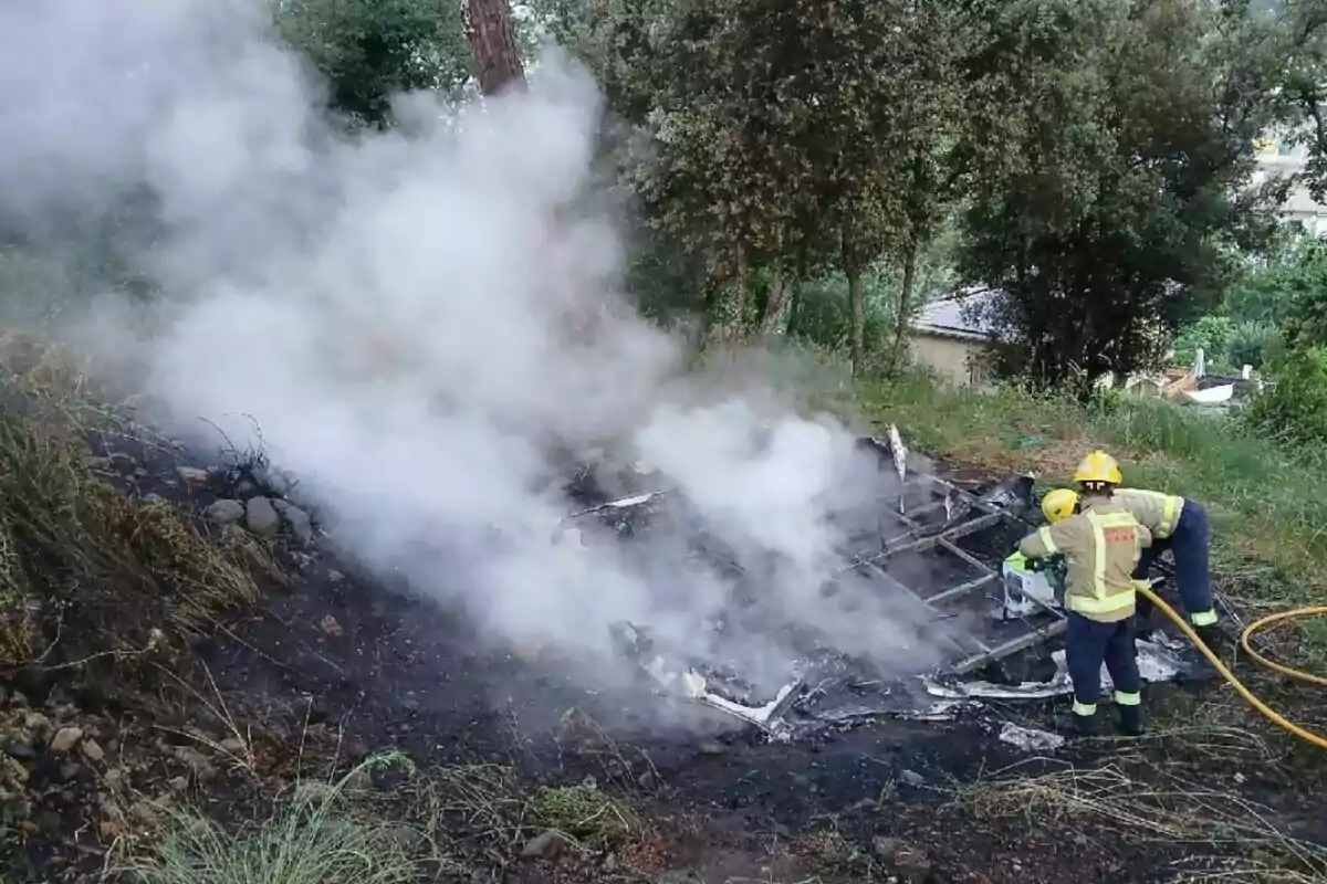 Dos bombers apaguen les restes fumejants d’un incendi en una zona boscosa
