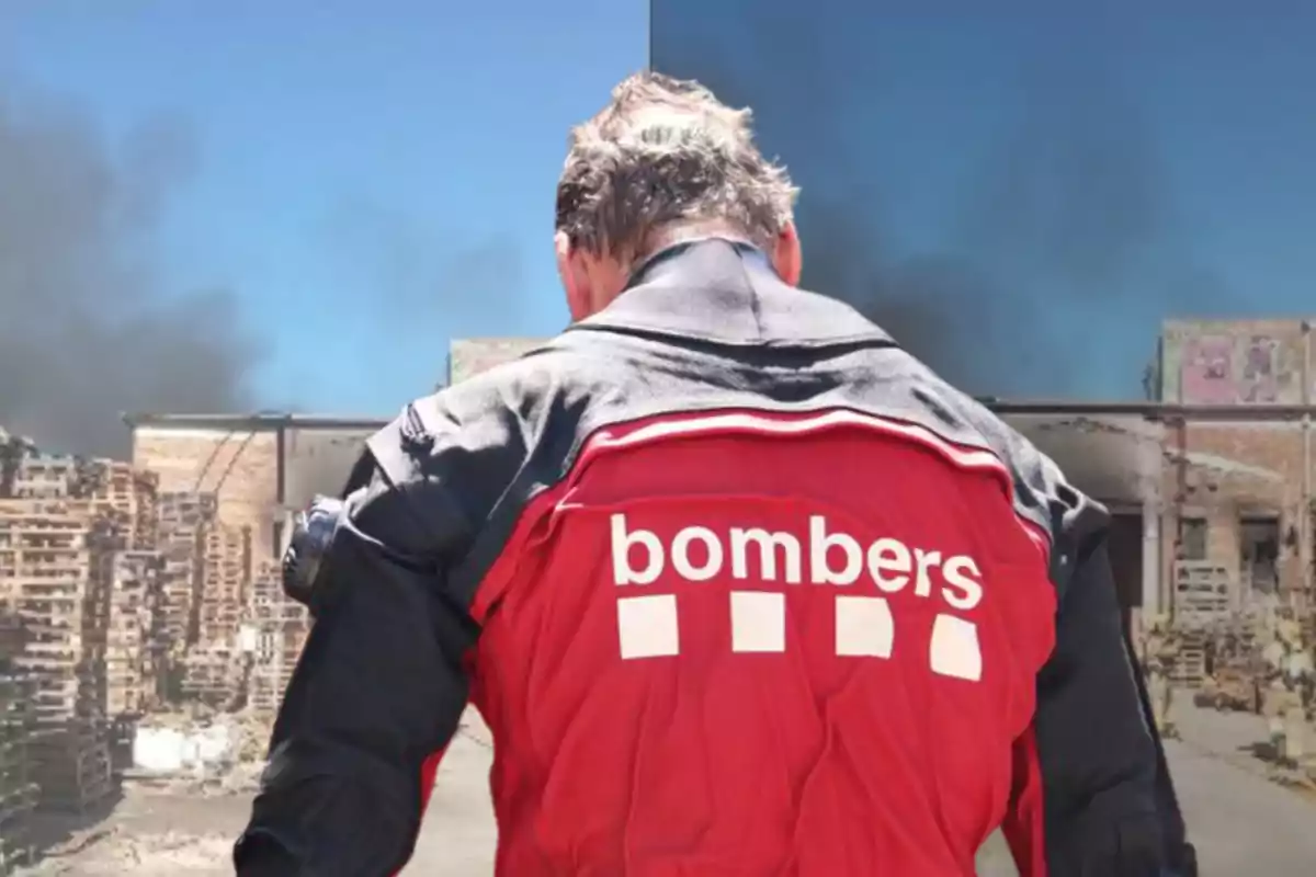 Persona d’esquena amb jaqueta vermella de bomber observant un incendi en un magatzem de palets de fusta