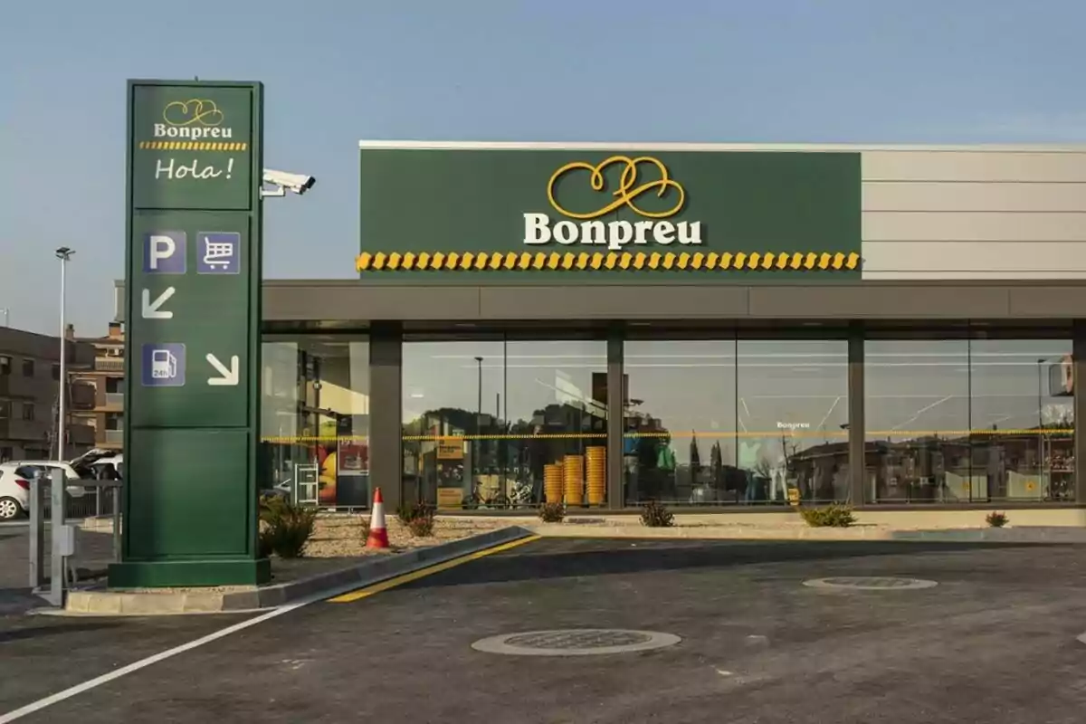 Façana d'un supermercat Bonpreu amb un rètol verd que diu "Hola!" i senyals d'estacionament, carretó de compres i benzinera.