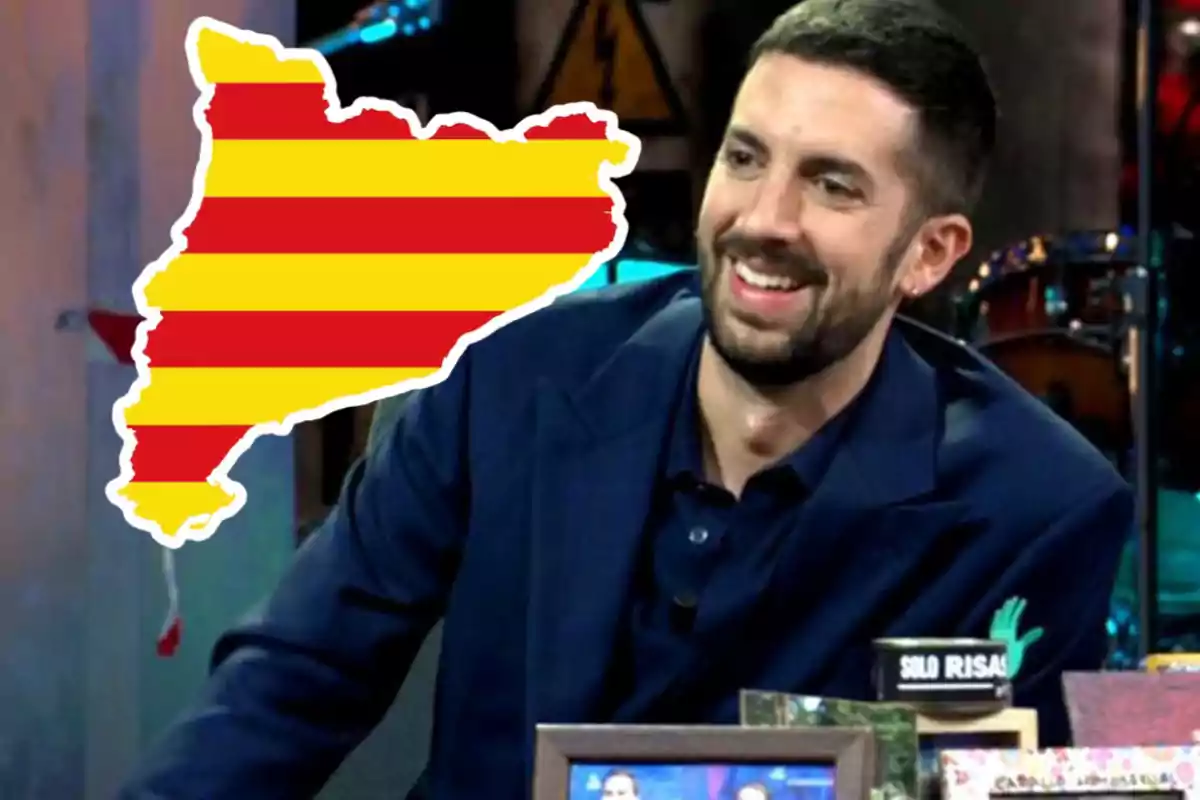 Un hombre sonriente con barba y cabello corto, vestido con un traje oscuro, está sentado en un estudio de televisión; a su lado, hay una ilustración del mapa de Cataluña con las franjas rojas y amarillas de la bandera catalana.
